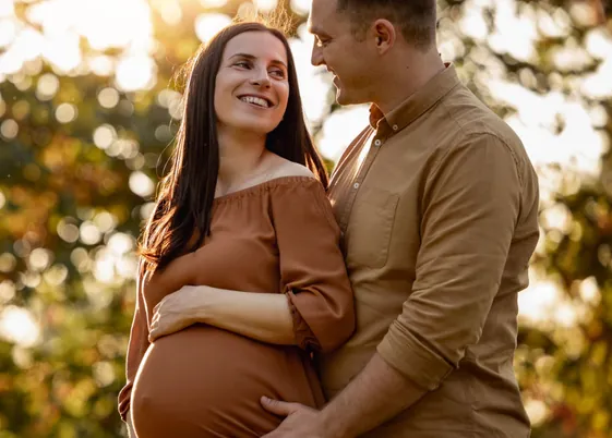 Casal com gestante sorrindo ao pôr do sol