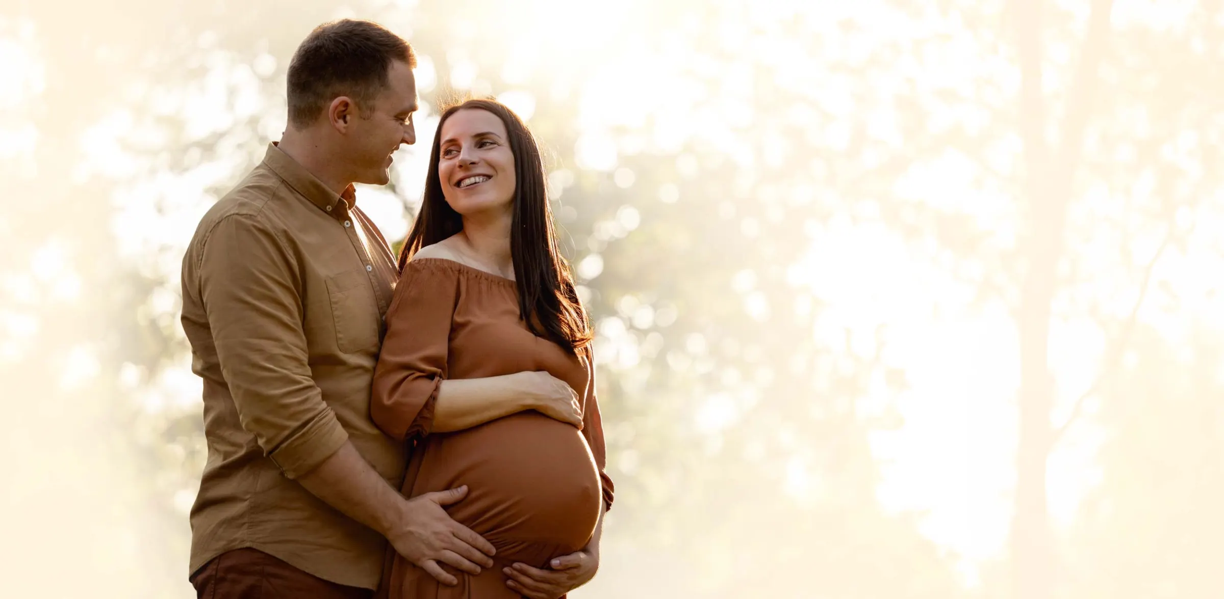 Casal à espera de um bebê sorrindo ao ar livre